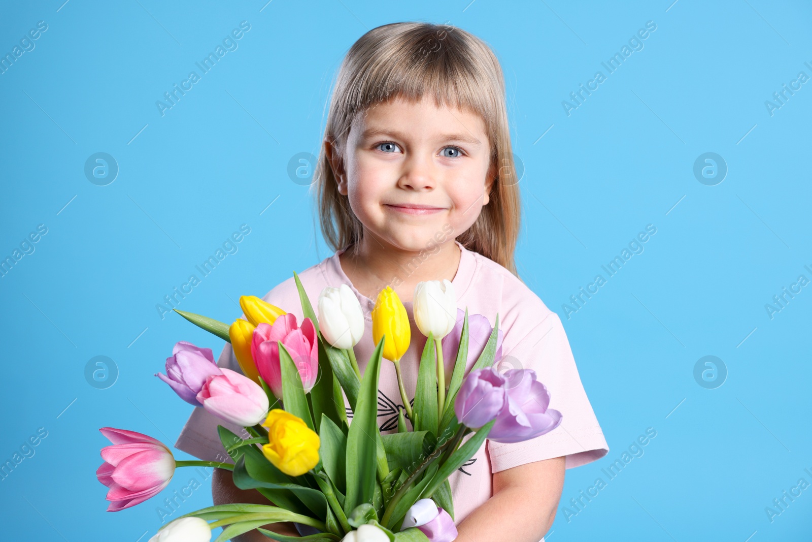 Photo of Cute little girl with bouquet of tulips on light blue background