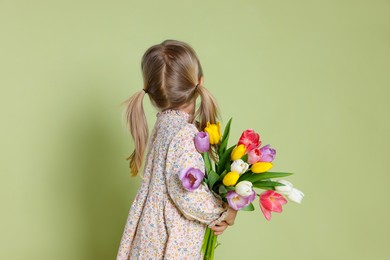 Photo of Little girl with bouquet of tulips on green background, back view