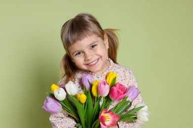 Photo of Smiling little girl with bouquet of tulips on green background