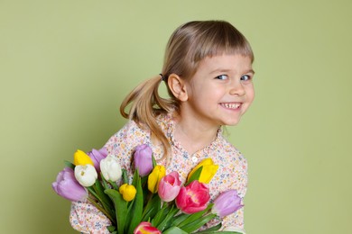 Photo of Smiling little girl with bouquet of tulips on green background