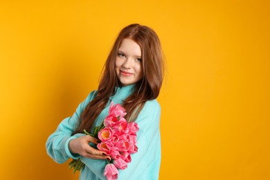 Photo of Beautiful teenage girl with bouquet of tulips on orange background