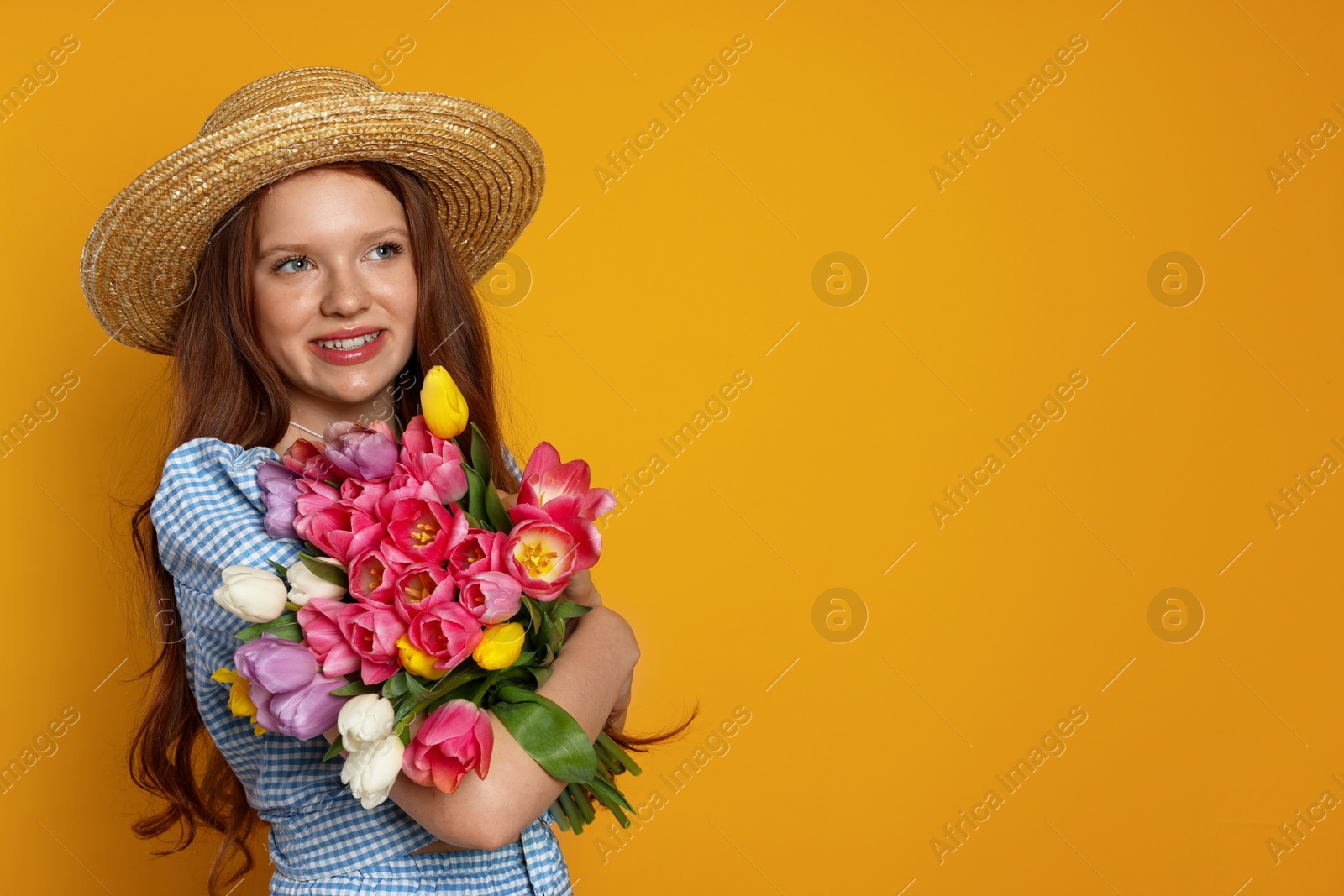 Photo of Beautiful teenage girl with bouquet of tulips on orange background, space for text