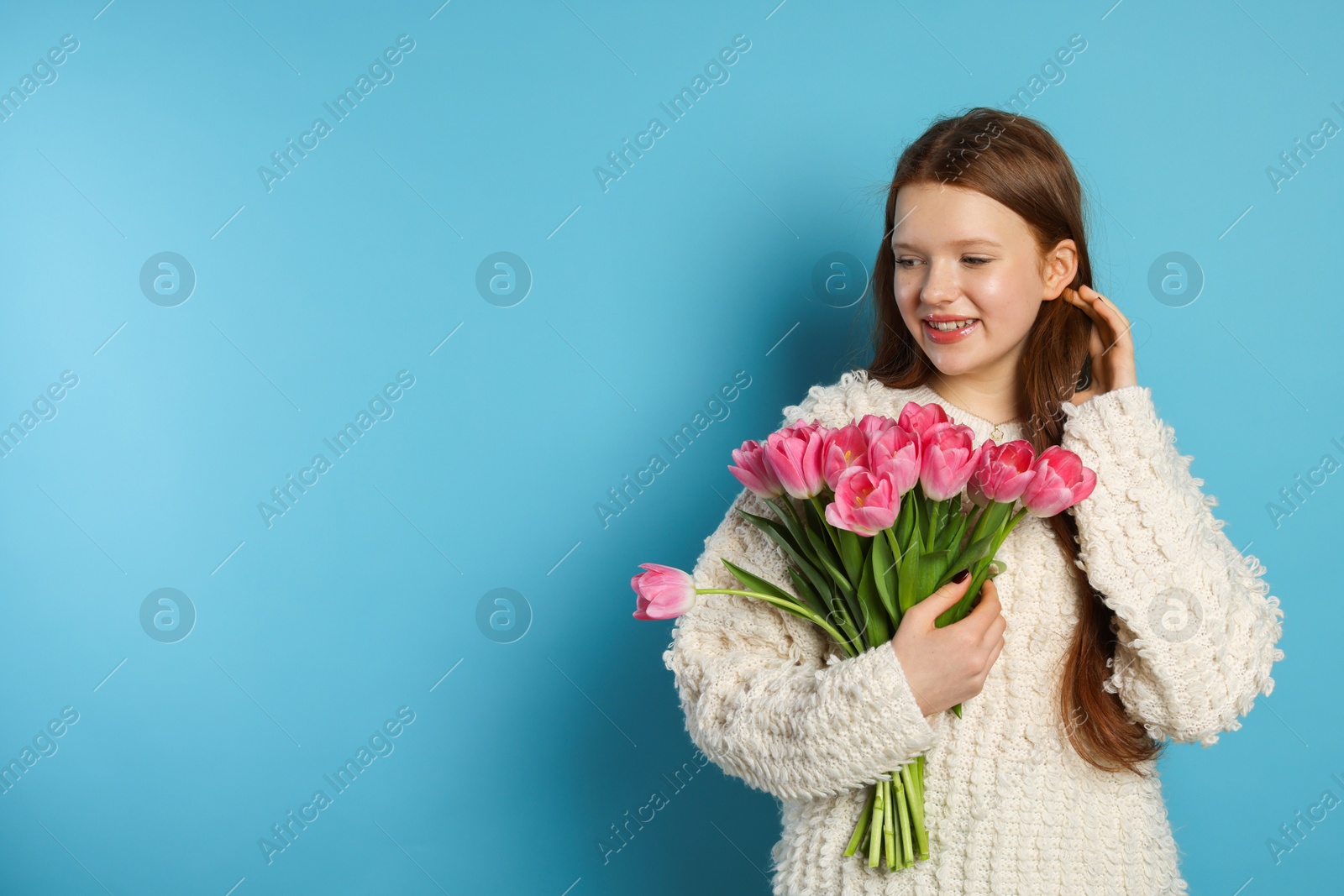 Photo of Beautiful teenage girl with bouquet of tulips on light blue background, space for text