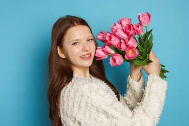 Photo of Beautiful teenage girl with bouquet of tulips on light blue background