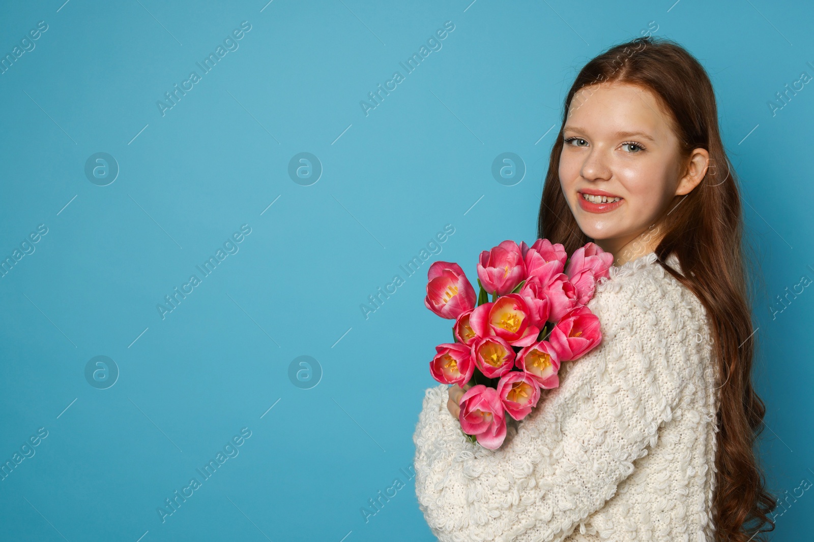 Photo of Beautiful teenage girl with bouquet of tulips on light blue background, space for text