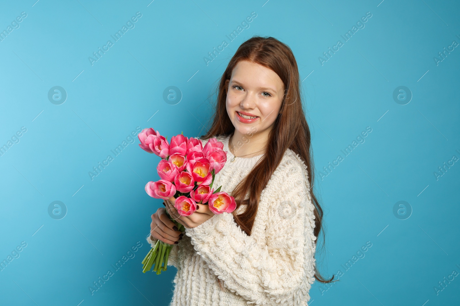 Photo of Beautiful teenage girl with bouquet of tulips on light blue background