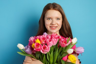 Photo of Beautiful teenage girl with bouquet of tulips on light blue background