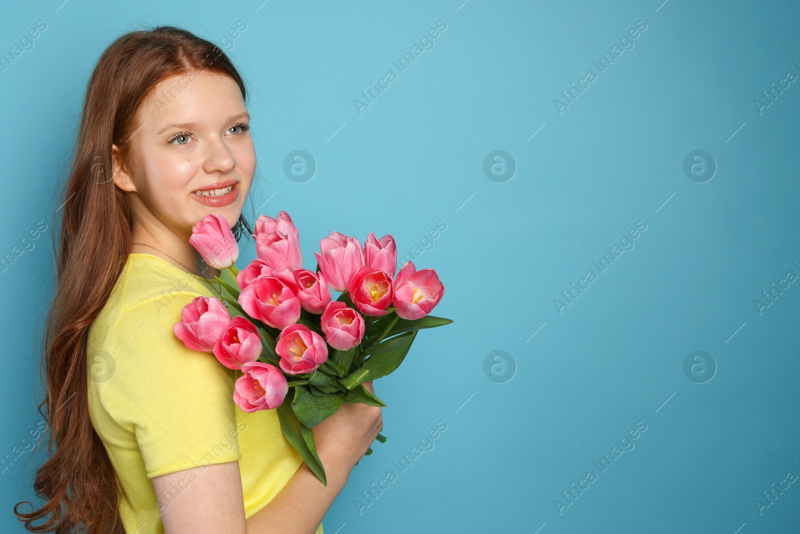 Photo of Beautiful teenage girl with bouquet of tulips on light blue background, space for text