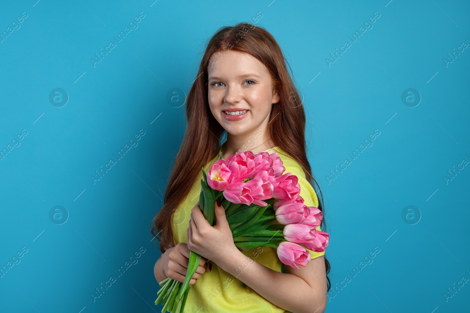 Photo of Beautiful teenage girl with bouquet of tulips on light blue background