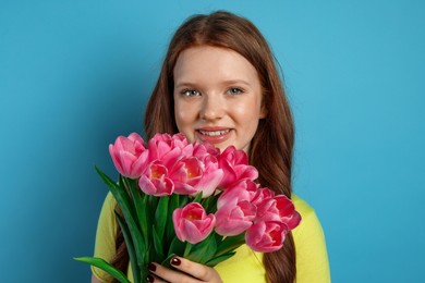 Photo of Beautiful teenage girl with bouquet of tulips on light blue background