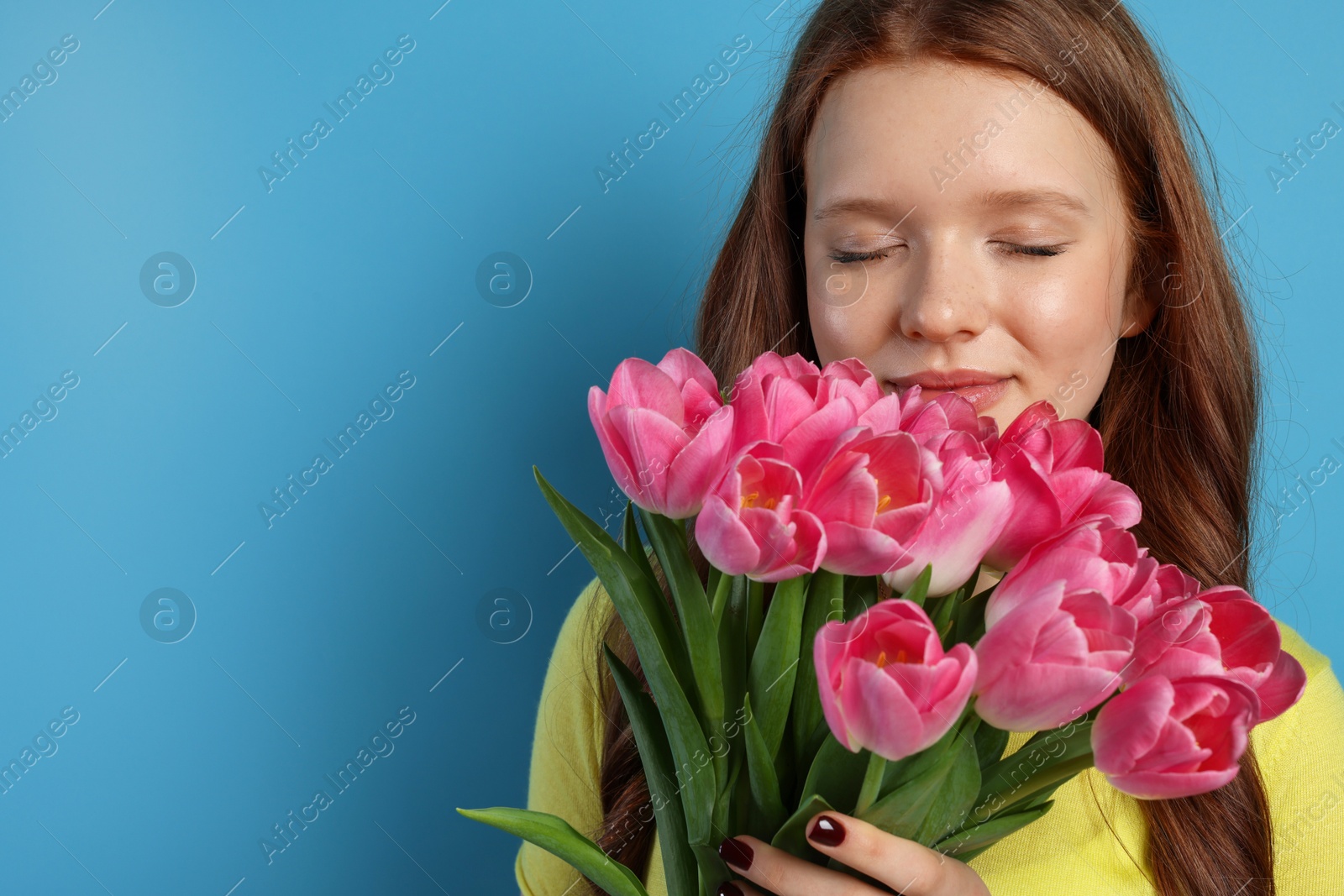 Photo of Beautiful teenage girl with bouquet of tulips on light blue background, space for text