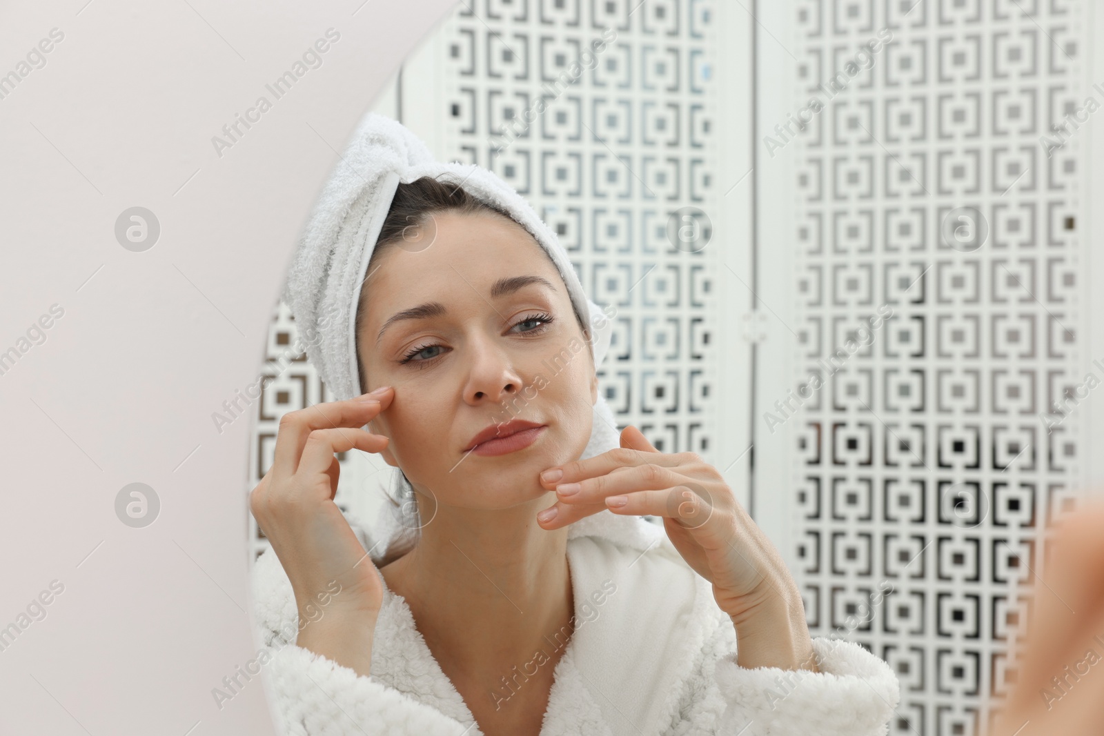 Photo of Spa day. Beautiful woman in bathrobe near mirror indoors