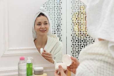 Photo of Spa day. Beautiful woman with cream near mirror indoors