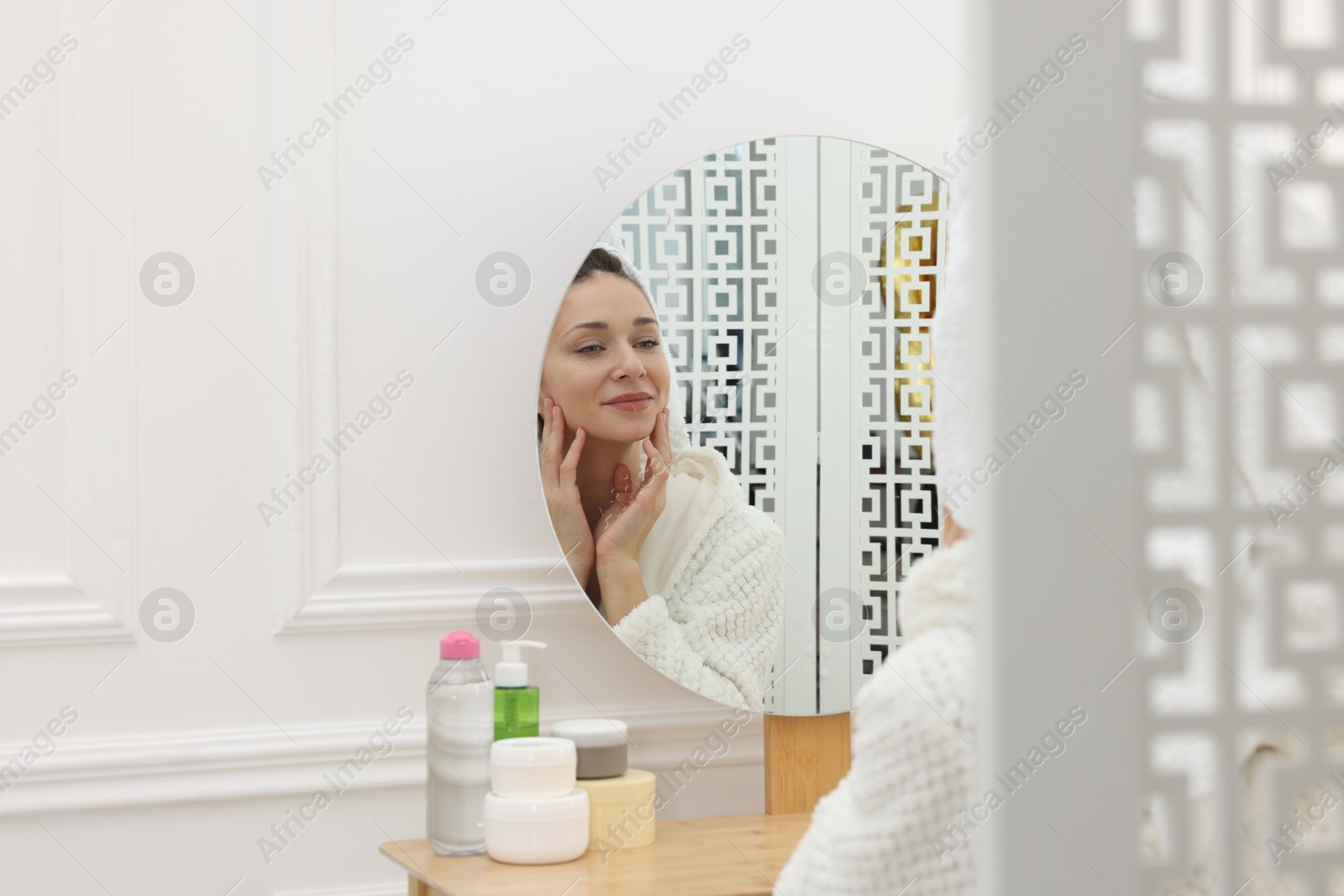 Photo of Spa day. Beautiful woman with towel on head near mirror indoors