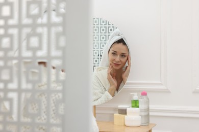 Photo of Spa day. Beautiful woman with towel on head near mirror indoors