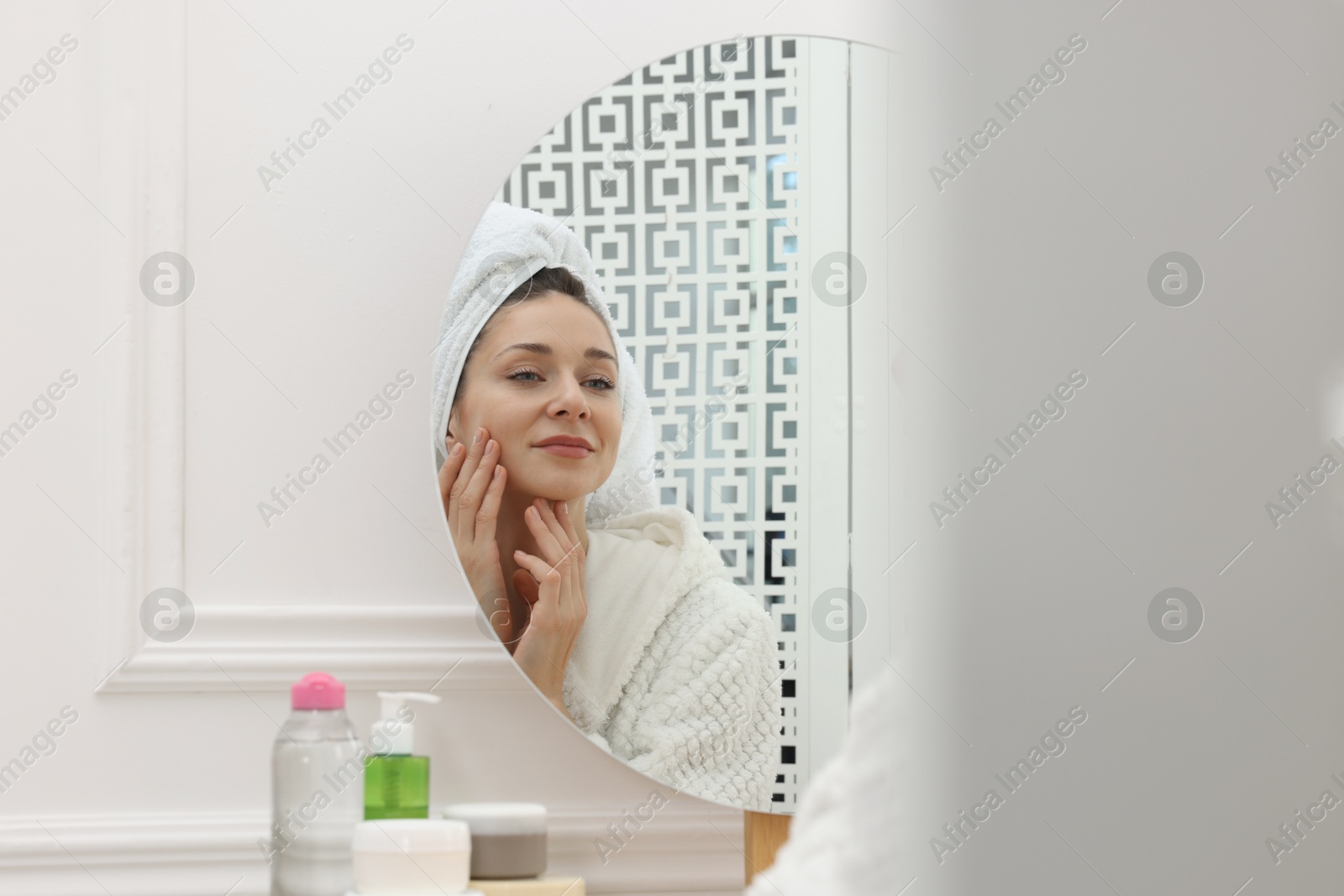 Photo of Spa day. Beautiful woman with towel on head near mirror indoors