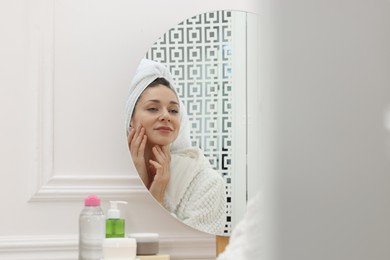 Photo of Spa day. Beautiful woman with towel on head near mirror indoors