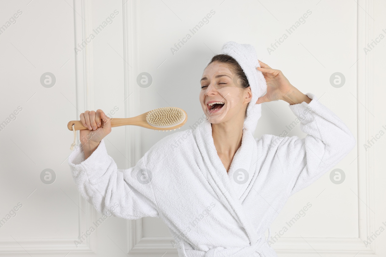 Photo of Spa day. Beautiful woman with face mask and brush singing indoors