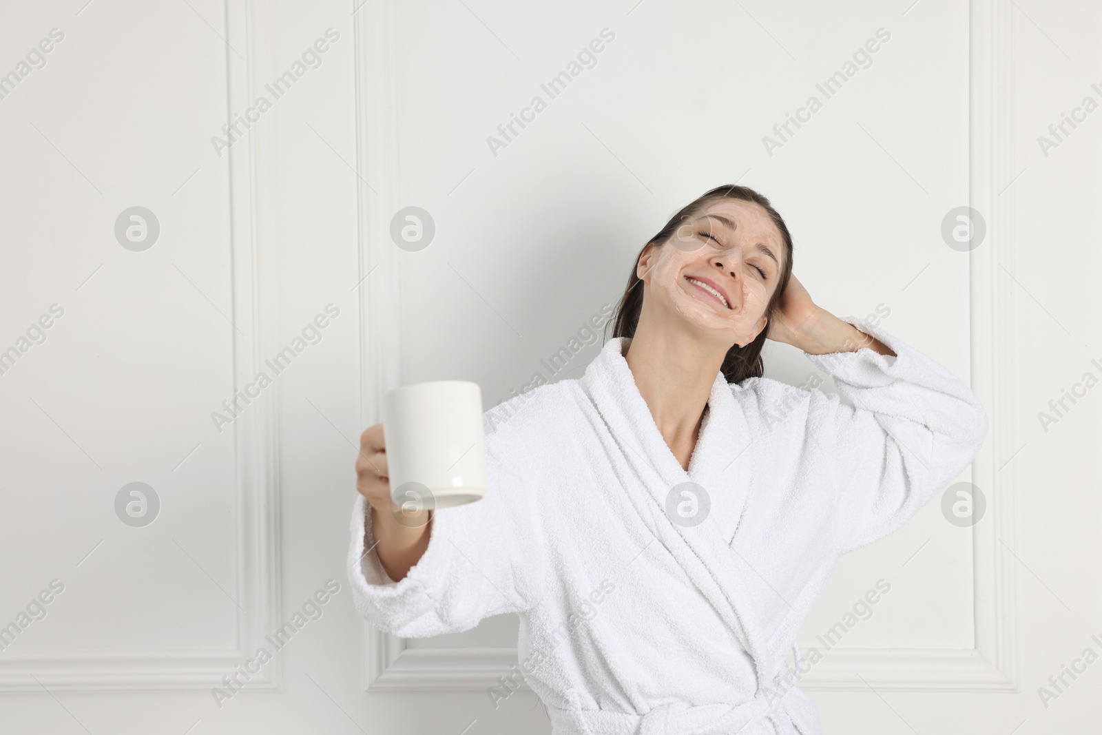 Photo of Spa day. Beautiful woman with face mask and cup of drink indoors, space for text