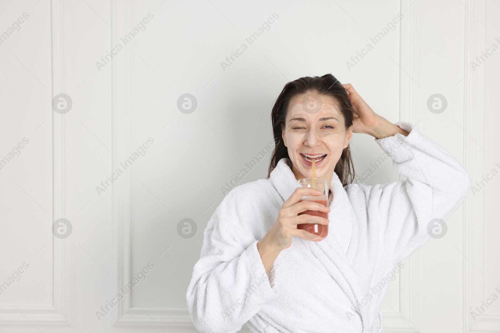 Photo of Spa day. Beautiful woman with face mask drinking juice indoors, space for text