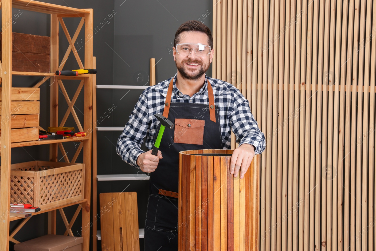 Photo of Relaxing hobby. Smiling man repairing wooden trash can with hammer in workshop