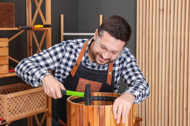 Photo of Relaxing hobby. Man repairing wooden trash can with hammer in workshop