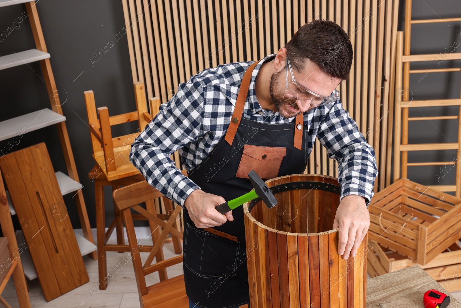 Photo of Relaxing hobby. Man repairing wooden trash can with hammer in workshop