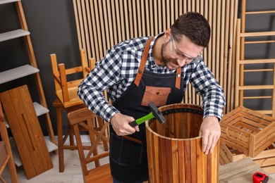 Photo of Relaxing hobby. Man repairing wooden trash can with hammer in workshop