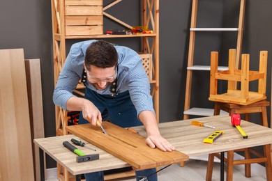 Photo of Relaxing hobby. Man working with wooden plank and chisel at table in workshop