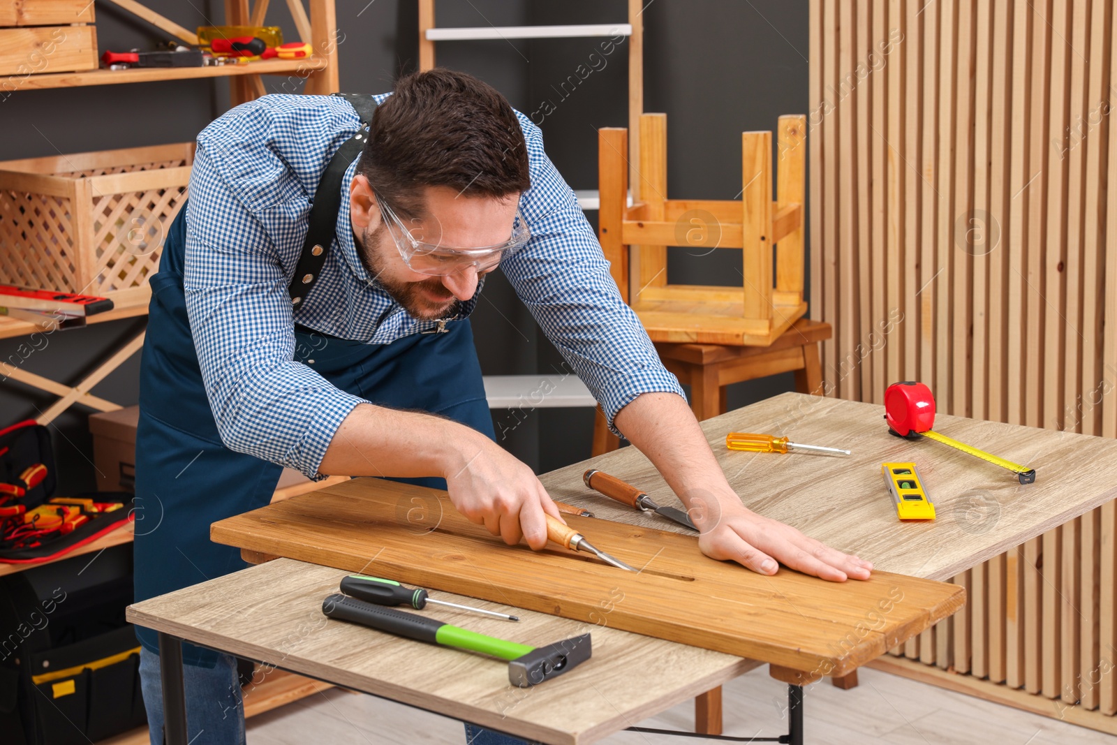 Photo of Relaxing hobby. Man working with wooden plank and chisel at table in workshop