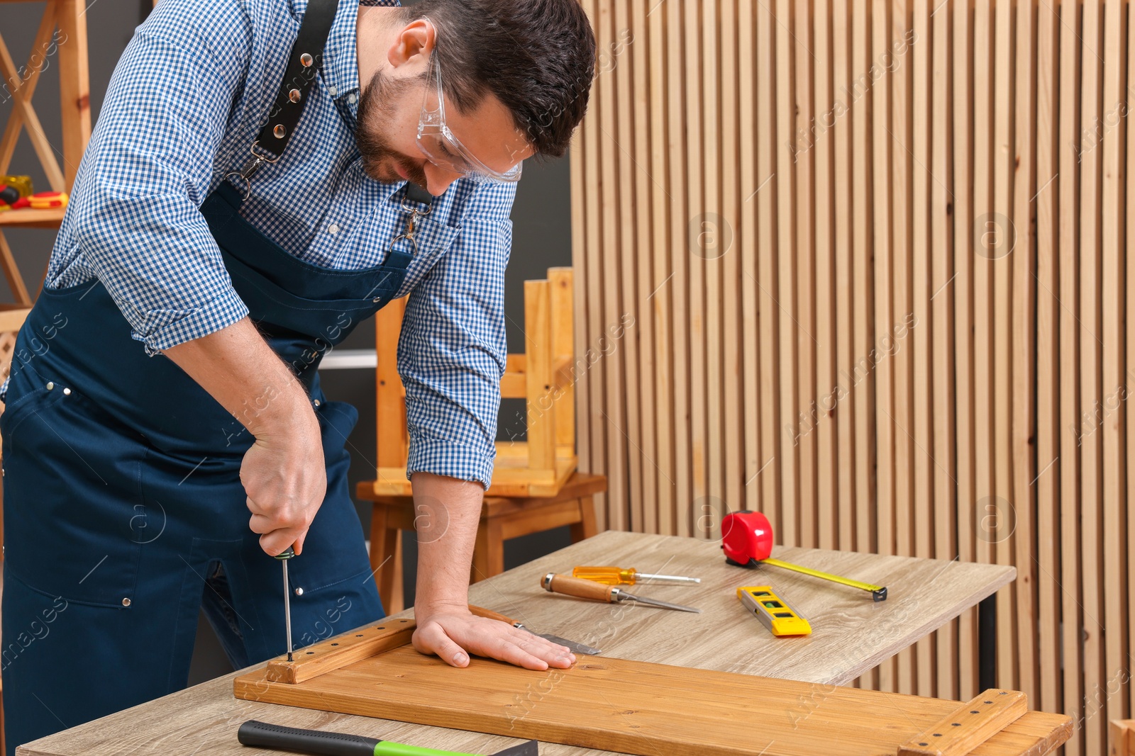 Photo of Relaxing hobby. Man working with wooden plank and screwdriver at table in workshop, space for text