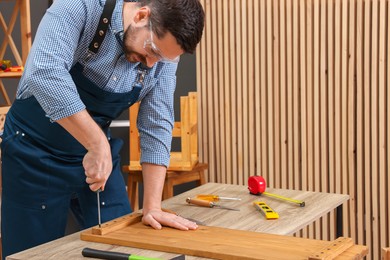 Photo of Relaxing hobby. Man working with wooden plank and screwdriver at table in workshop, space for text