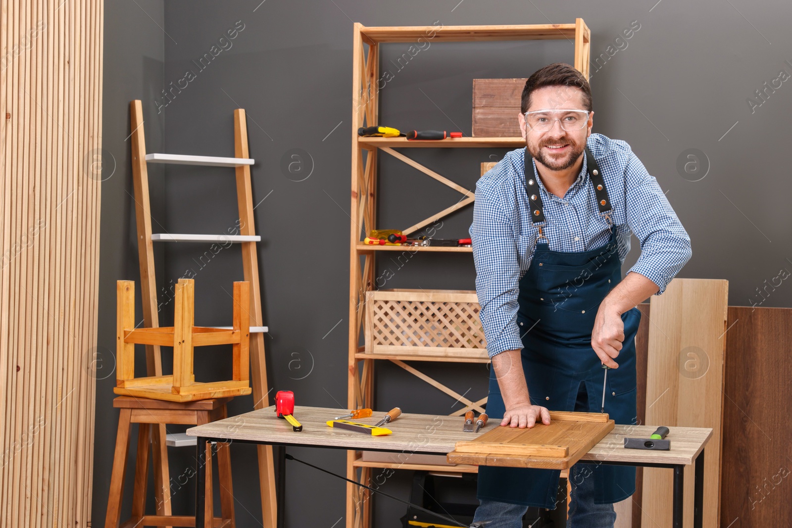 Photo of Relaxing hobby. Smiling man working with wooden plank and screwdriver at table in workshop