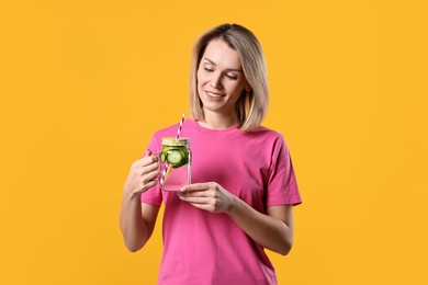 Photo of Woman with mason jar of water with cucumber on orange background. Refreshing drink