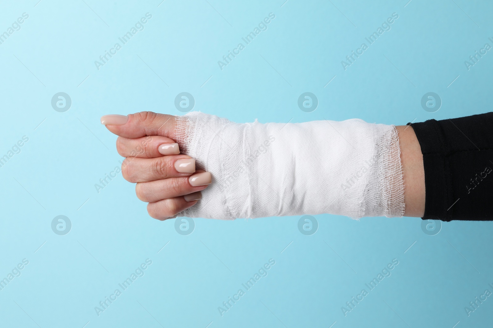 Photo of Woman with medical bandage on wrist against light blue background, closeup