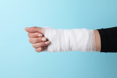 Photo of Woman with medical bandage on wrist against light blue background, closeup