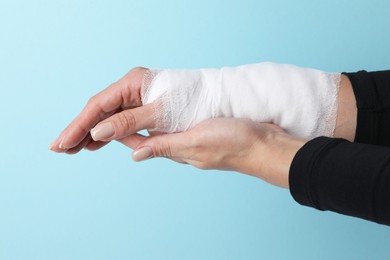 Photo of Woman with medical bandage on wrist against light blue background, closeup