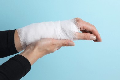 Photo of Woman with medical bandage on wrist against light blue background, closeup