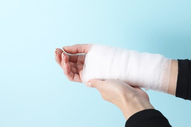 Photo of Woman with medical bandage on wrist against light blue background, closeup