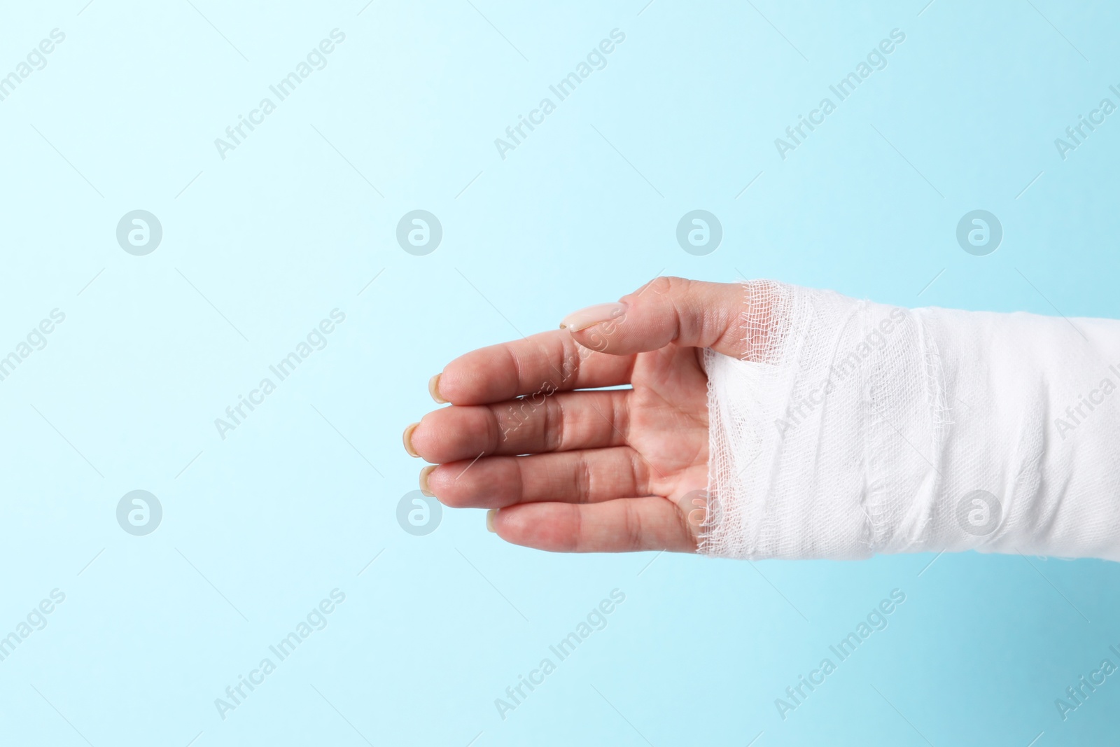 Photo of Woman with medical bandage on wrist against light blue background, closeup. Space for text