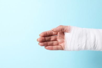 Photo of Woman with medical bandage on wrist against light blue background, closeup. Space for text