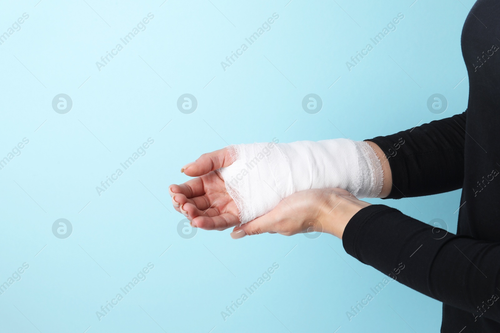 Photo of Woman with medical bandage on wrist against light blue background, closeup. Space for text