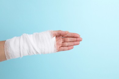 Photo of Woman with medical bandage on wrist against light blue background, closeup