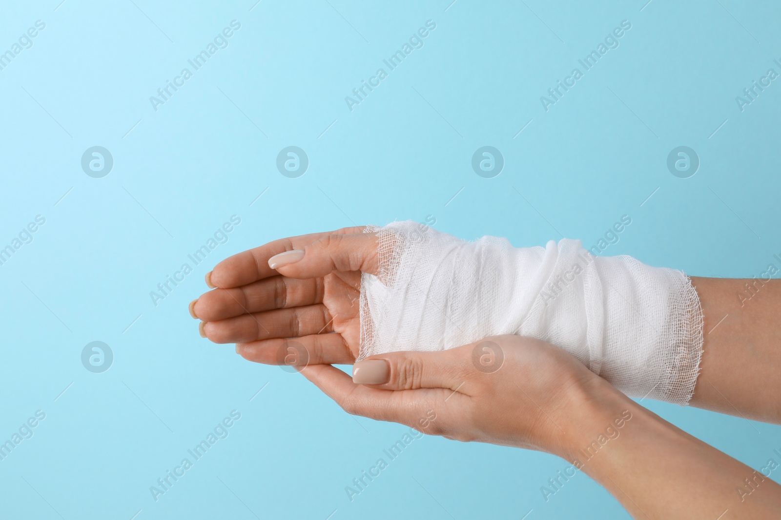 Photo of Woman with medical bandage on wrist against light blue background, closeup