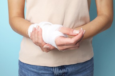 Photo of Woman with medical bandage on wrist against light blue background, closeup