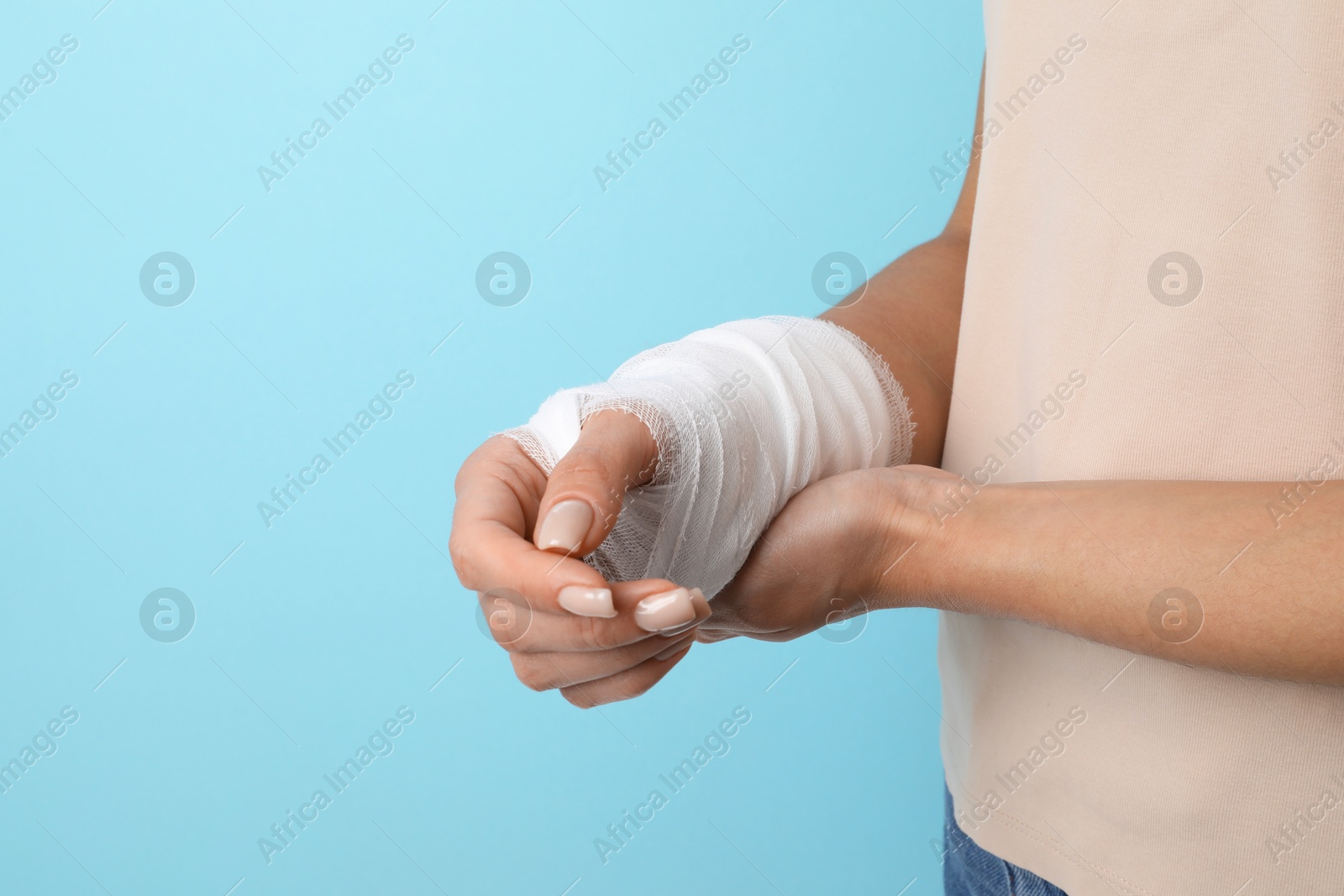 Photo of Woman with medical bandage on wrist against light blue background, closeup