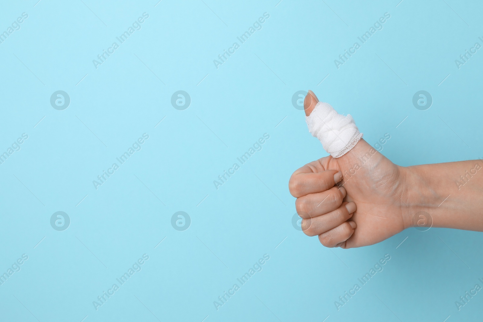 Photo of Woman with medical bandage on finger showing thumbs up against light blue background, closeup. Space for text