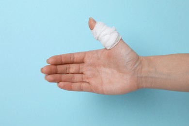 Photo of Woman with medical bandage on finger showing thumbs up against light blue background, closeup