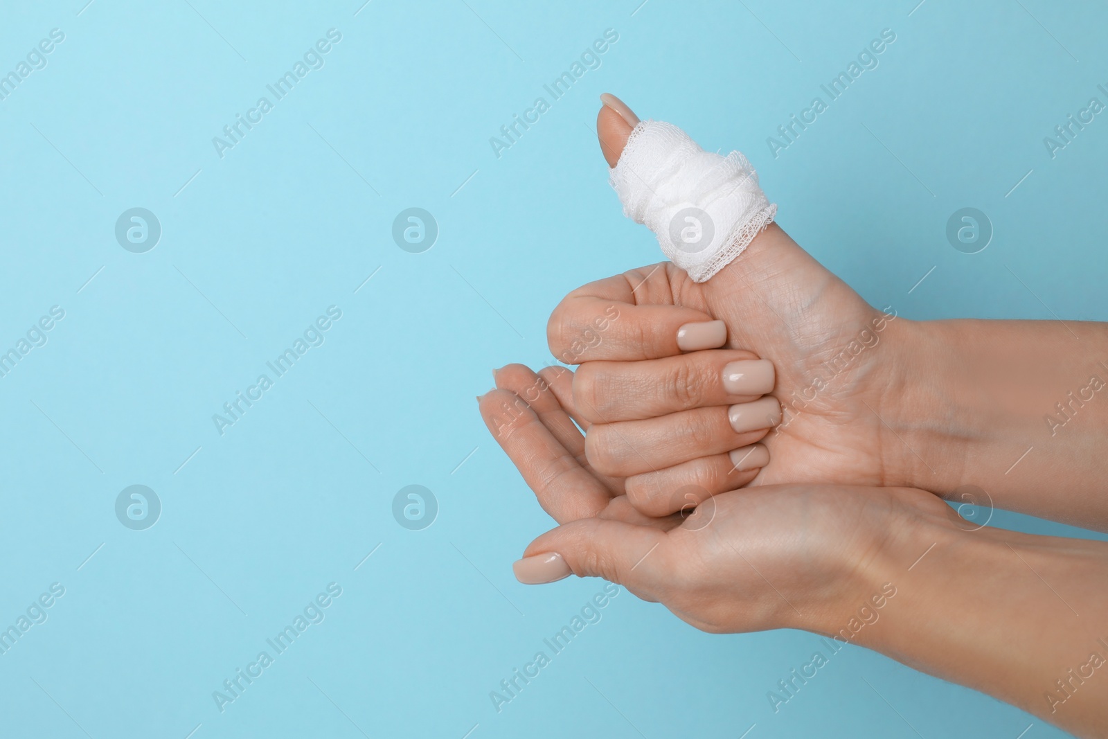 Photo of Woman with medical bandage on finger showing thumbs up against light blue background, closeup. Space for text