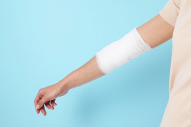 Photo of Woman with medical bandage on elbow against light blue background, closeup. Space for text